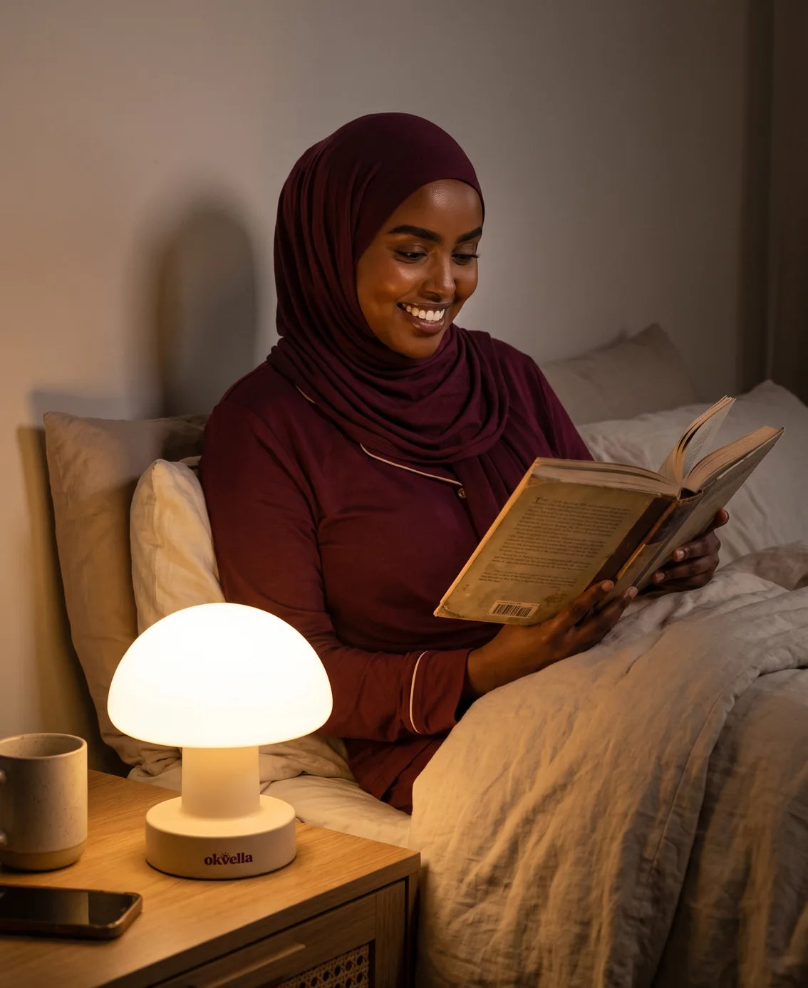Woman in a hijab reading in bed by the okvella bedside light