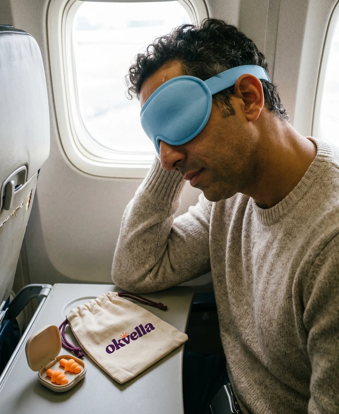 Man resting in an airplane seat with the okvella travel kit on the tray table